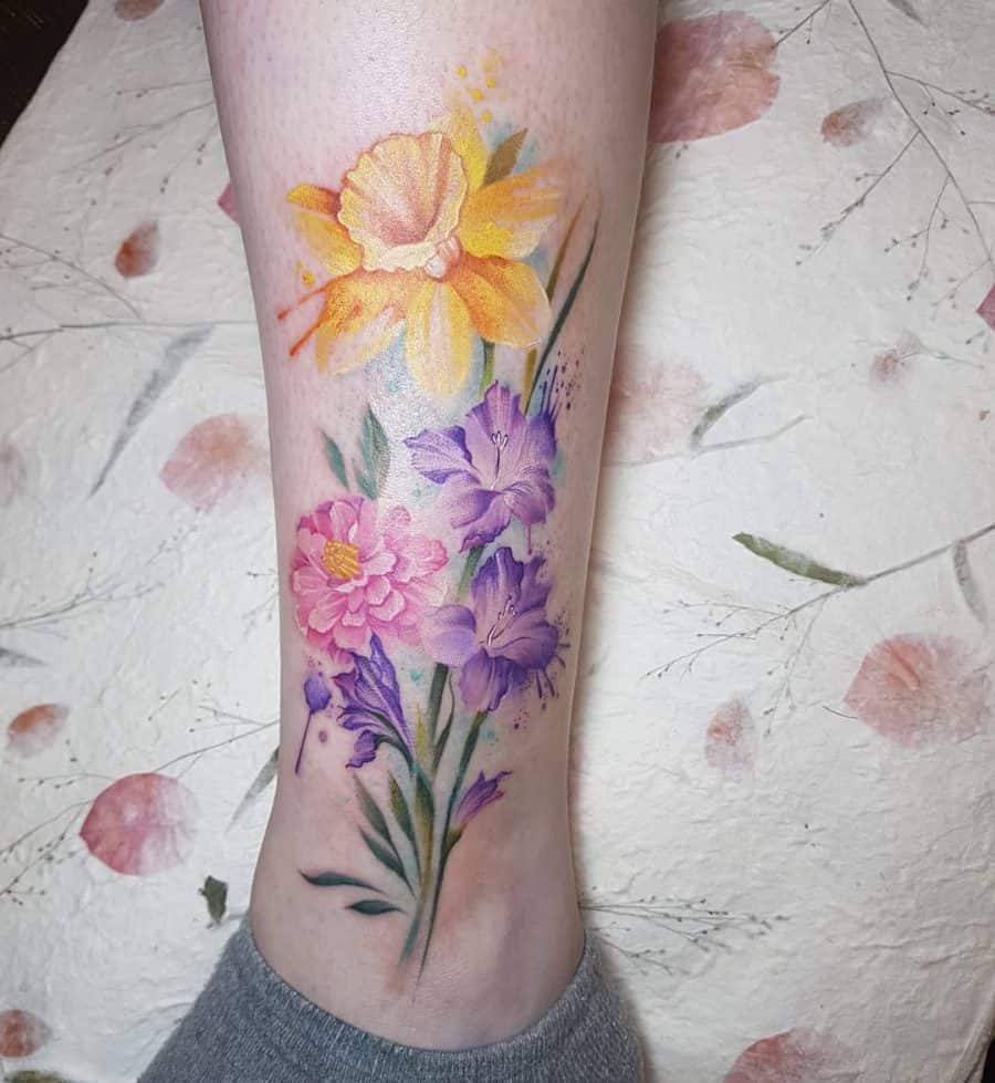A vibrant, watercolor-style tattoo featuring a daffodil in yellow, complemented by pink and purple flowers, blending soft hues with a delicate, floral design.