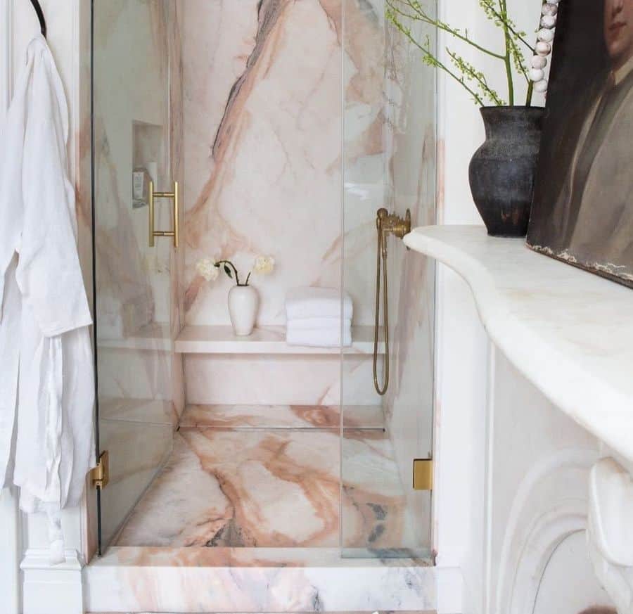 Pink marble shower with gold fixtures, glass door, and minimalist decor.