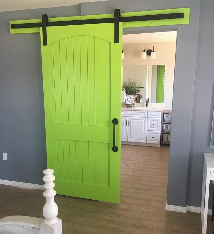 Bright green sliding barn door with arched top in a modern bedroom leading to a bathroom.