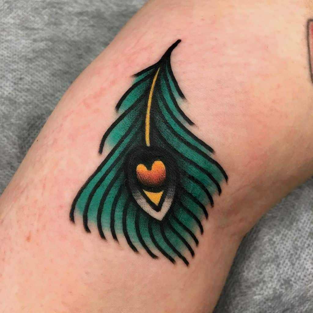 Bold and colorful peacock feather tattoo with a heart-shaped eye design, featuring rich green, black, and gold tones in a traditional tattoo style.