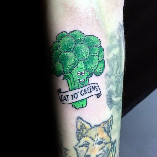 Colorful cartoon broccoli tattoo with a smiling face and a banner reading "Eat Yo’ Greens," promoting a fun and lighthearted design.