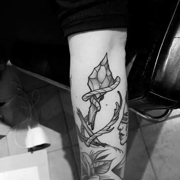 Black and grey broken arrow tattoo with a crystal tip and natural elements like leaves and branches wrapping around the design.