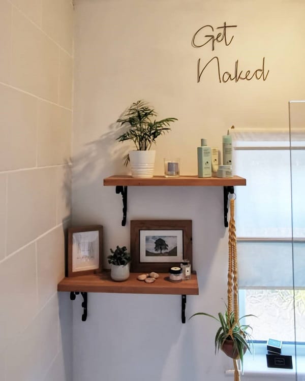 Bathroom with wooden floating shelves, black brackets, potted plants, and framed artwork.