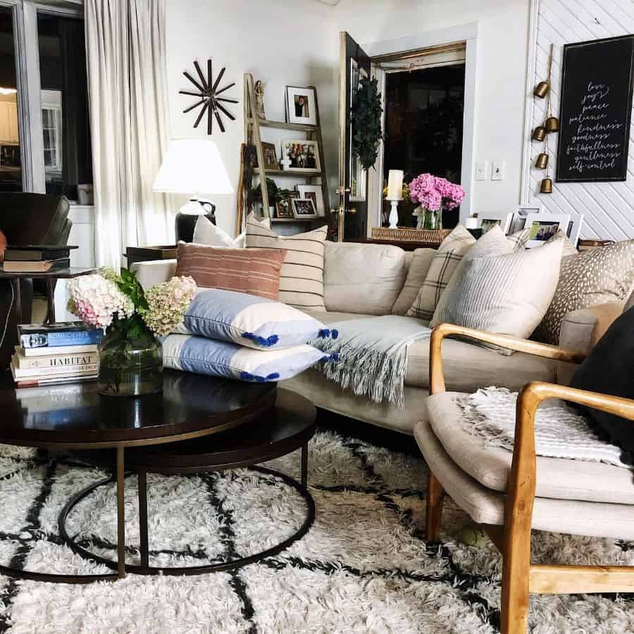 Cozy living room with neutral sofa, patterned rug, round coffee table, decorative pillows, and fresh flowers.