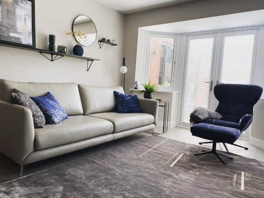Modern living room with grey sofa, blue accent chair, wall shelves, and large bay window.
