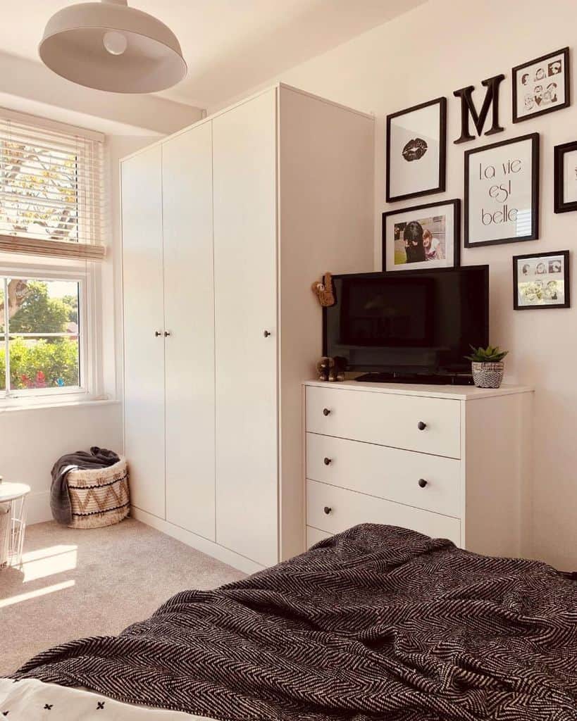 White wardrobe and dresser in cozy bedroom with gallery wall and window.