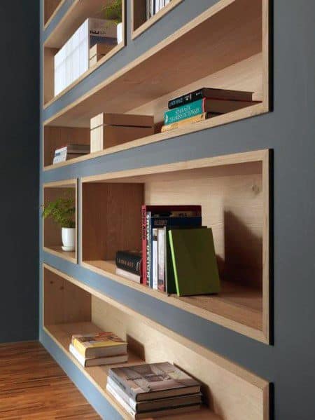 Modern built-in bookcase with wooden shelves and a gray backdrop, showcasing books, plants, and minimalist decor