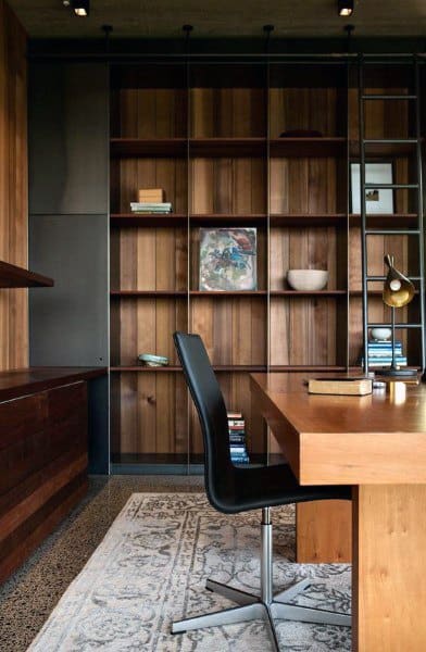 A modern home office with a wooden desk, black chair, shelving, books, and a decorative rug