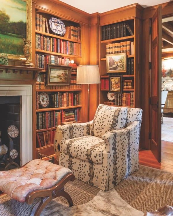 Warm wood-paneled library with built-in bookshelves, a cozy armchair, and a fireplace.