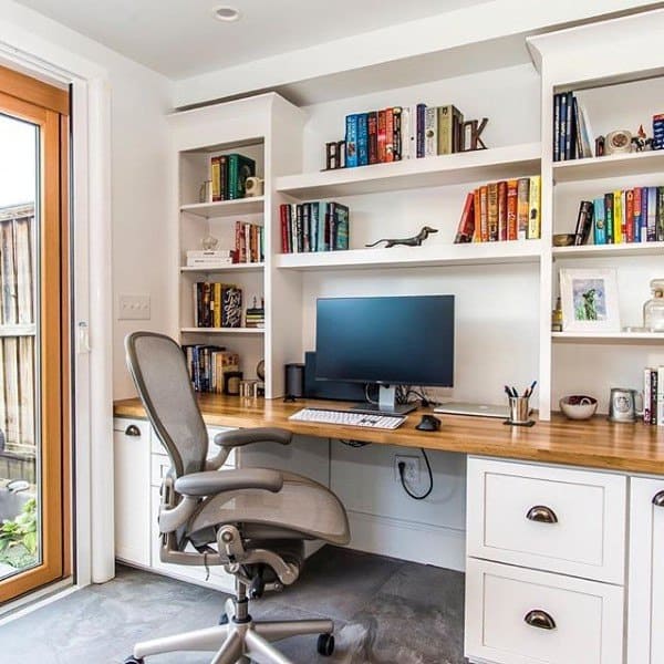 Home office with a built-in desk, ergonomic chair, computer, and bookshelves filled with colorful books and decor