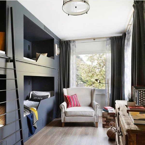 Cozy room with dark bunk beds, a comfy armchair, large window, and wooden dresser; perfect for bunk style living