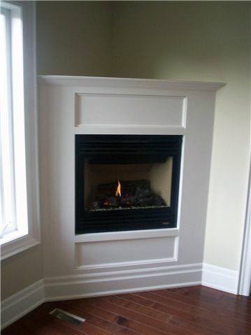Minimalist corner fireplace with white mantel and dark wood flooring.