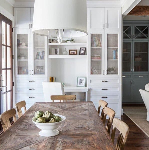 Dining area with a wooden table, chairs, built-in desk, white cabinetry, books, decor, and a white chandelier