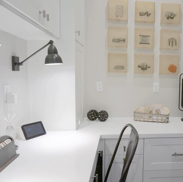 Minimalistic home office with a white built-in desk, metal chair, wall art, and a small tablet on the surface