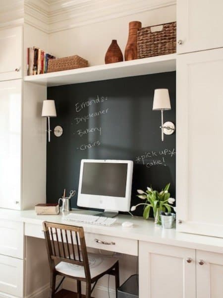 Home office with a built-in desk, chalkboard wall, computer, tulips, and decor items on shelves