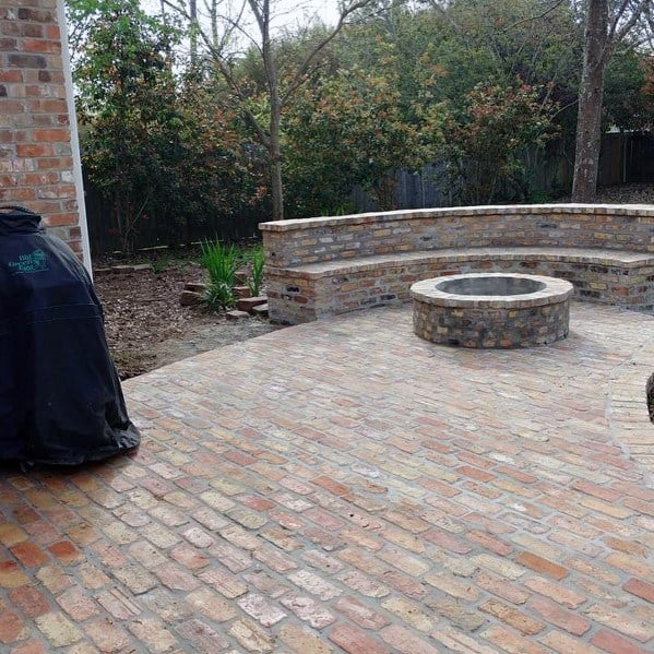 Brick patio with circular fire pit, and built-in bench nestled among trees