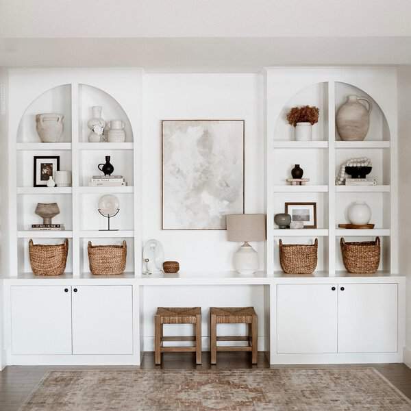 White built-in shelves with arched tops, woven baskets, and neutral-toned decorative accents.