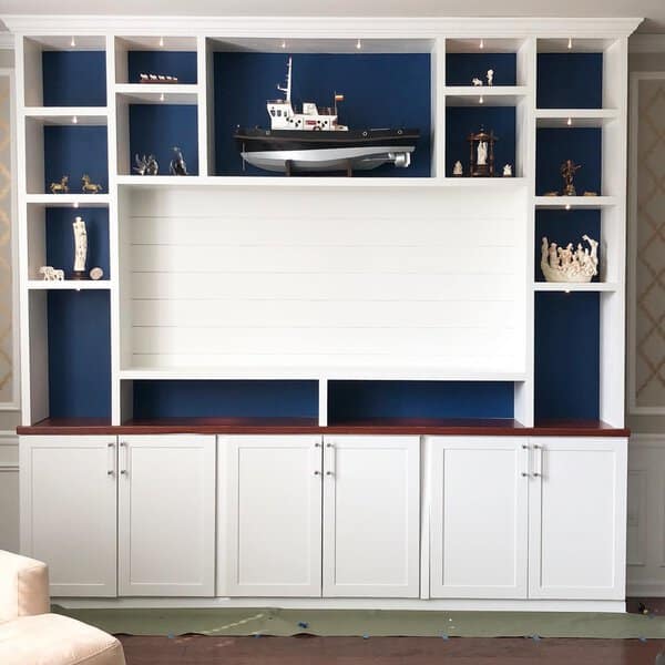 Custom white built-in shelves with navy backing, display lighting, and decorative accents.