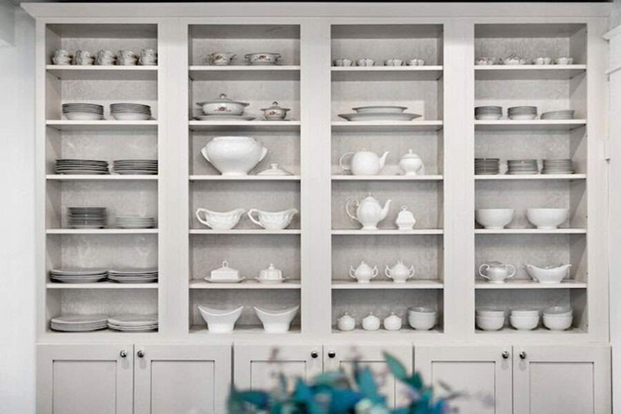 Elegant built-in shelves displaying fine china, porcelain teapots, and neatly stacked plates.