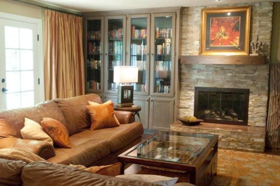 Cozy living room with glass-front built-in bookshelves, stone fireplace, and warm-toned decor.