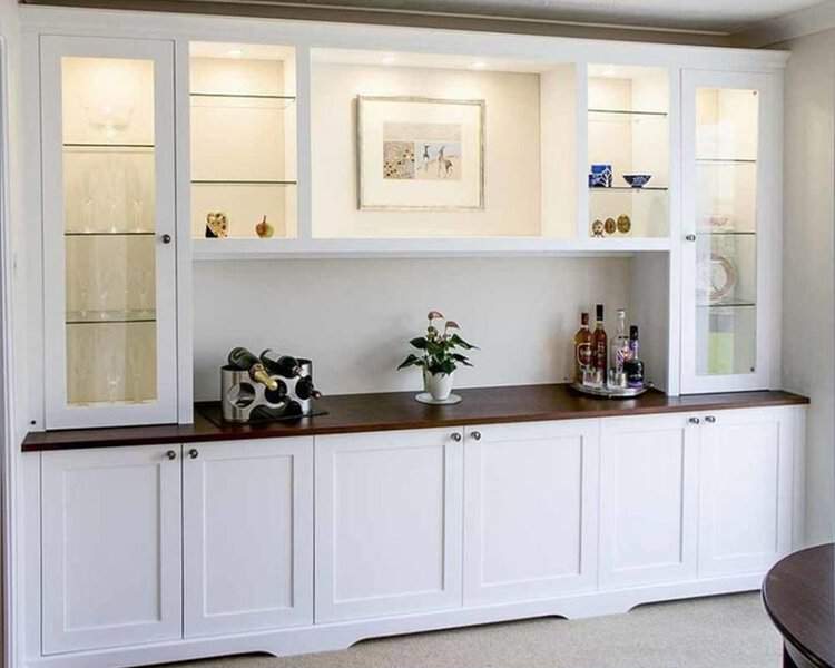 White built-in cabinet with glass display shelves, wood countertop, and soft interior lighting.