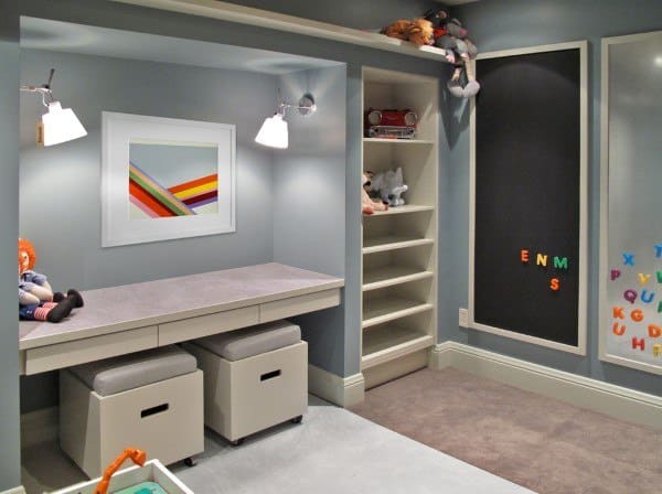 Children's playroom with gray walls, art, and chalkboard; built-in desk with stools, colorful letters, shelves, and toys