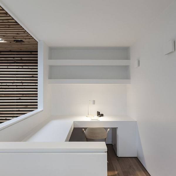 Minimalist white office with built-in desk, chair, and shelf, next to a window with a wooden slat wall outside
