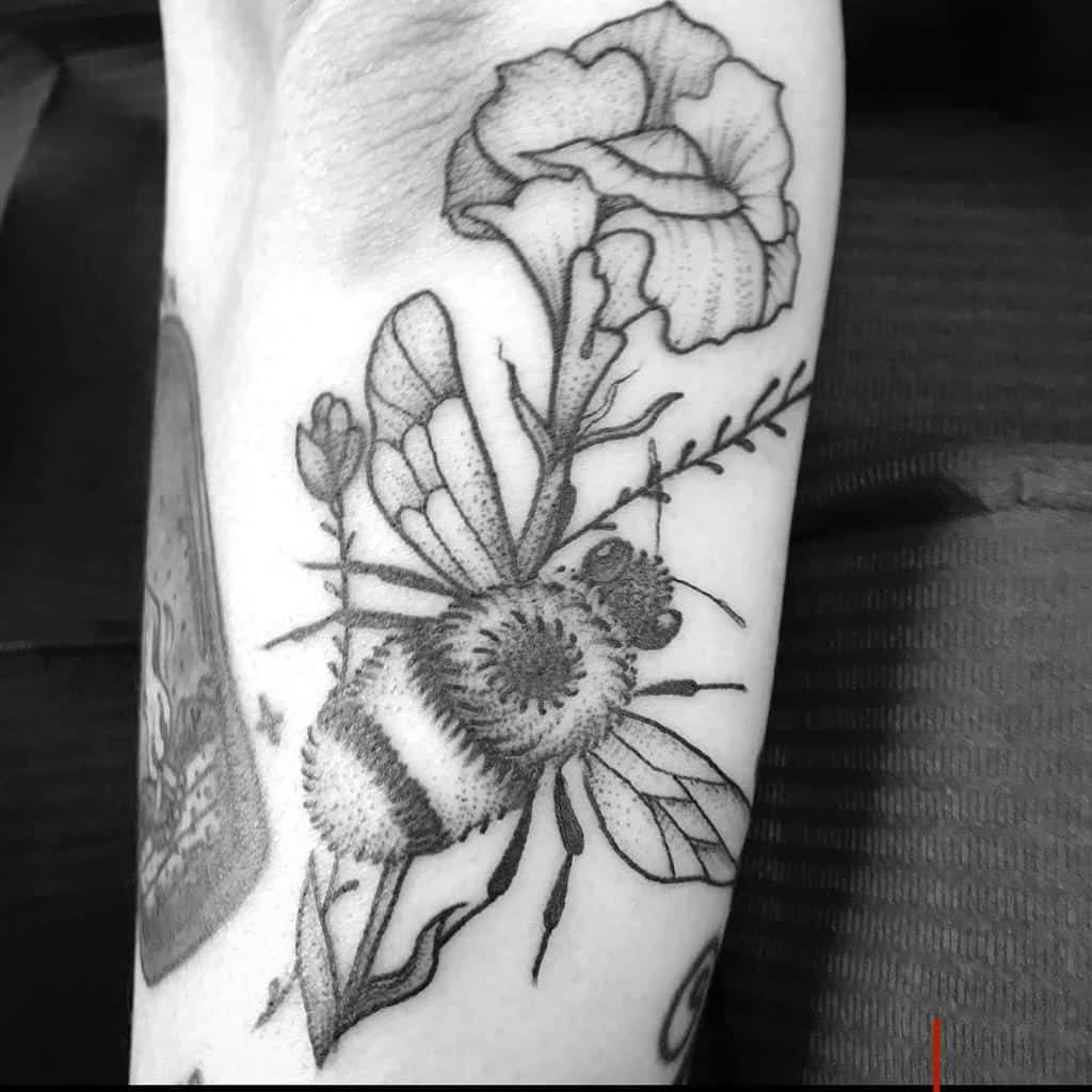 Black and white tattoo of a bee next to a large carnation with leaves