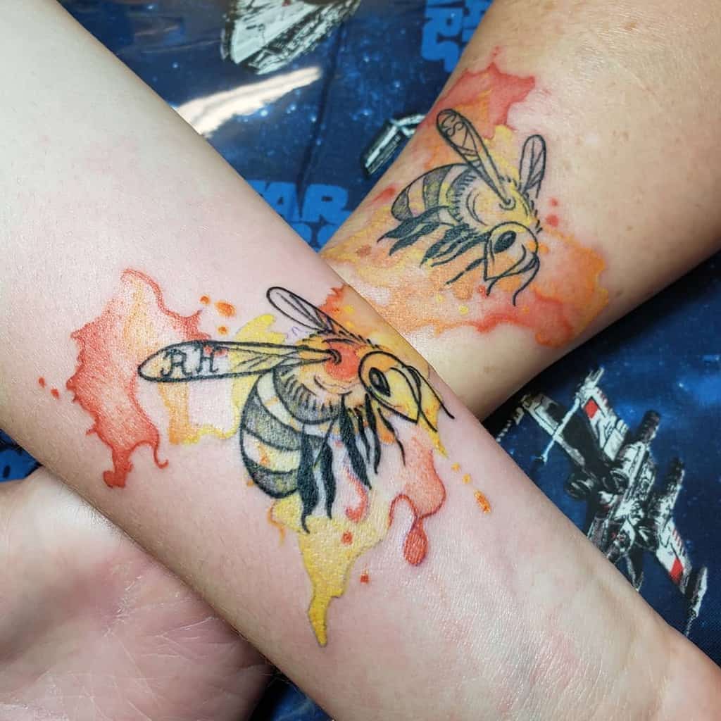 Matching bumblebee mother-daughter tattoos featuring vibrant watercolor splashes