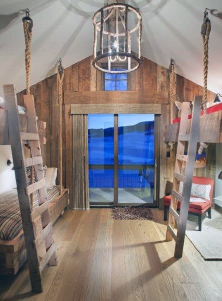 Rustic bedroom with hanging bunk beds, rope supports, and wooden walls overlooking a scenic view.