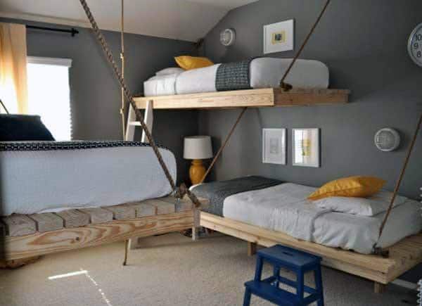 Room with suspended wooden bunk beds, gray walls, and yellow pillows; ladder stool for bunk access