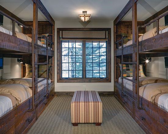 Rustic bunk bed room with dark wood frames, metal railings, cozy bedding, and a central ottoman for a warm, cabin vibe