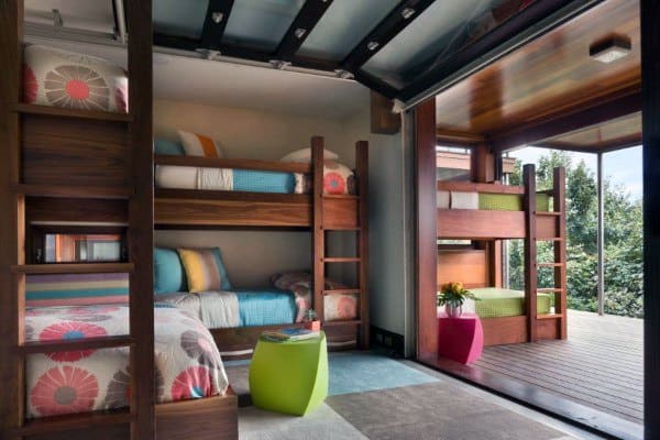 Modern bunk beds with colorful bedding, wooden frames, and an open-air design connecting to a scenic outdoor space