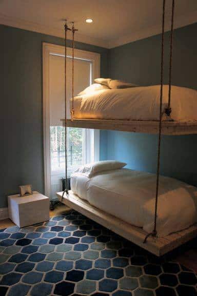 A small room with blue walls, featuring suspended bunk beds and a geometric patterned rug