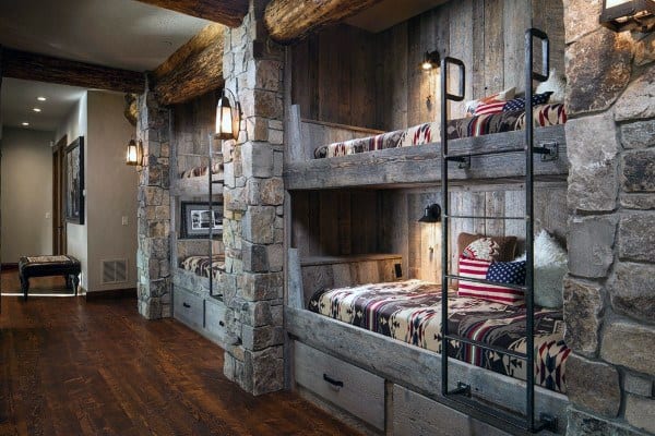 Rustic room with stone walls features built-in bunk beds, ladders, and cozy lighting