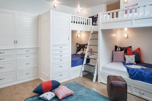 Cozy bedroom with white bunk beds, blue bedding, pillows, a ladder, and a small wooden chest on a bunk blue rug