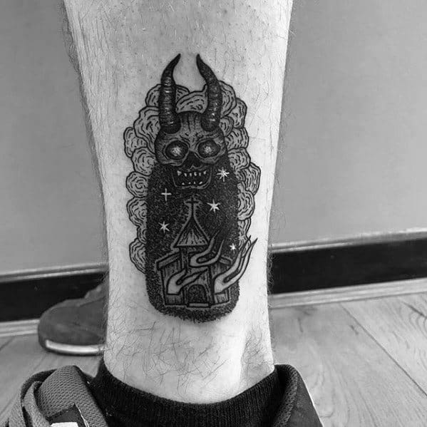 Dark burning church tattoo with flames and stars beneath a horned skull figure. Surrounded by swirling smoke on lower leg.