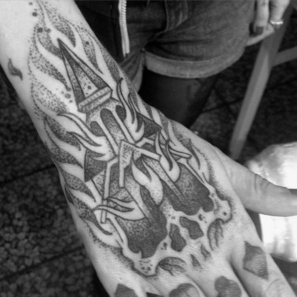 Burning church tattoo on the hand with bold lines and dotwork shading. Flames rise from the structure above a skull silhouette.