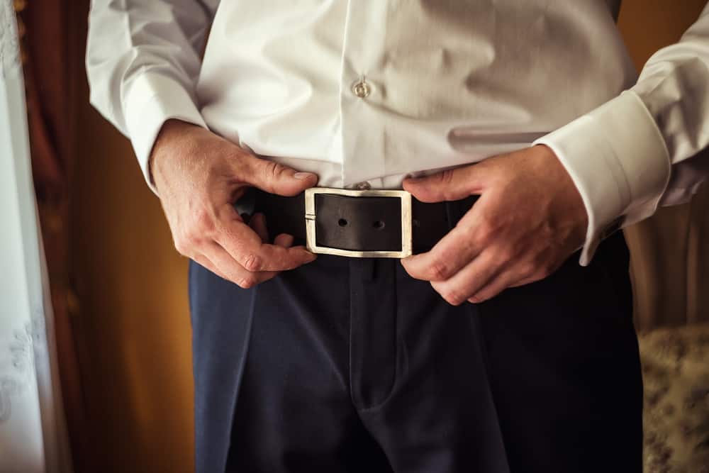 businessman putting belt on blue pant