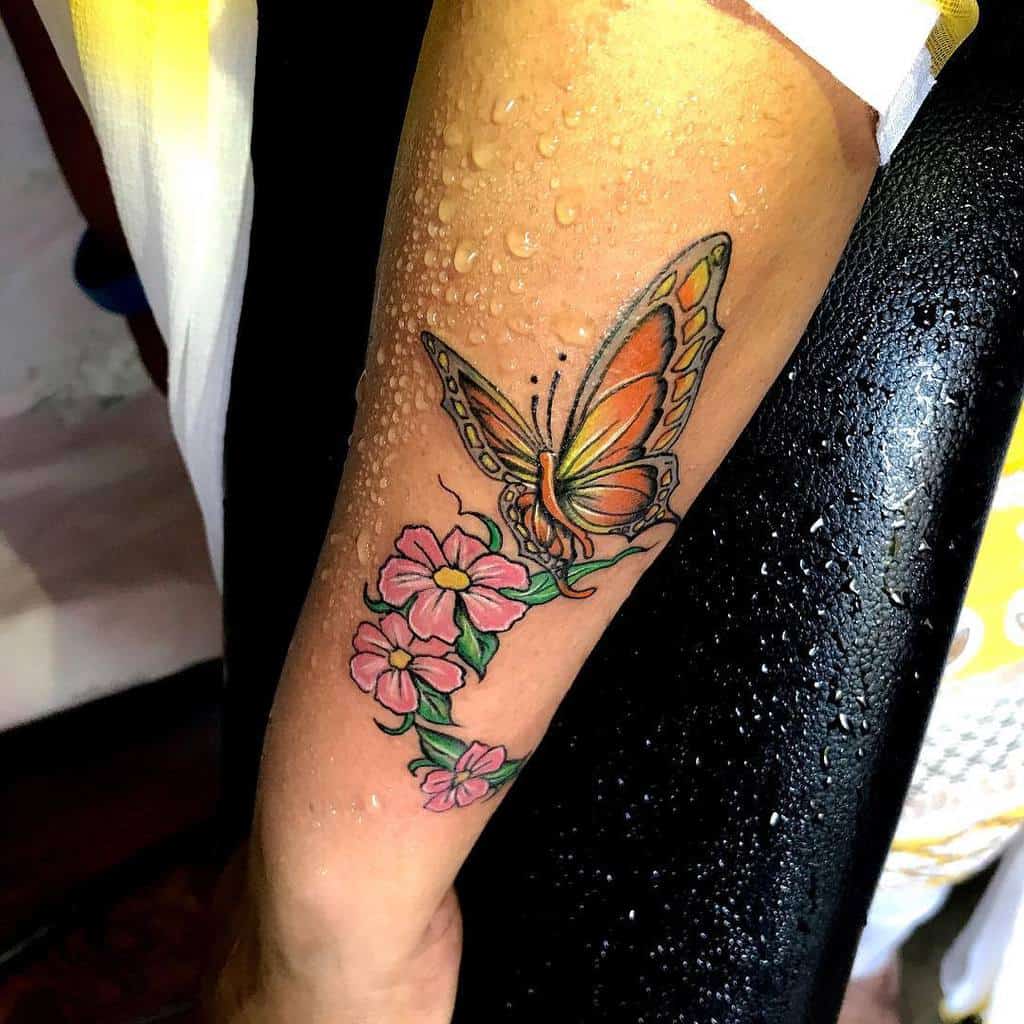 A colorful butterfly tattoo with flowers on a woman's forearm