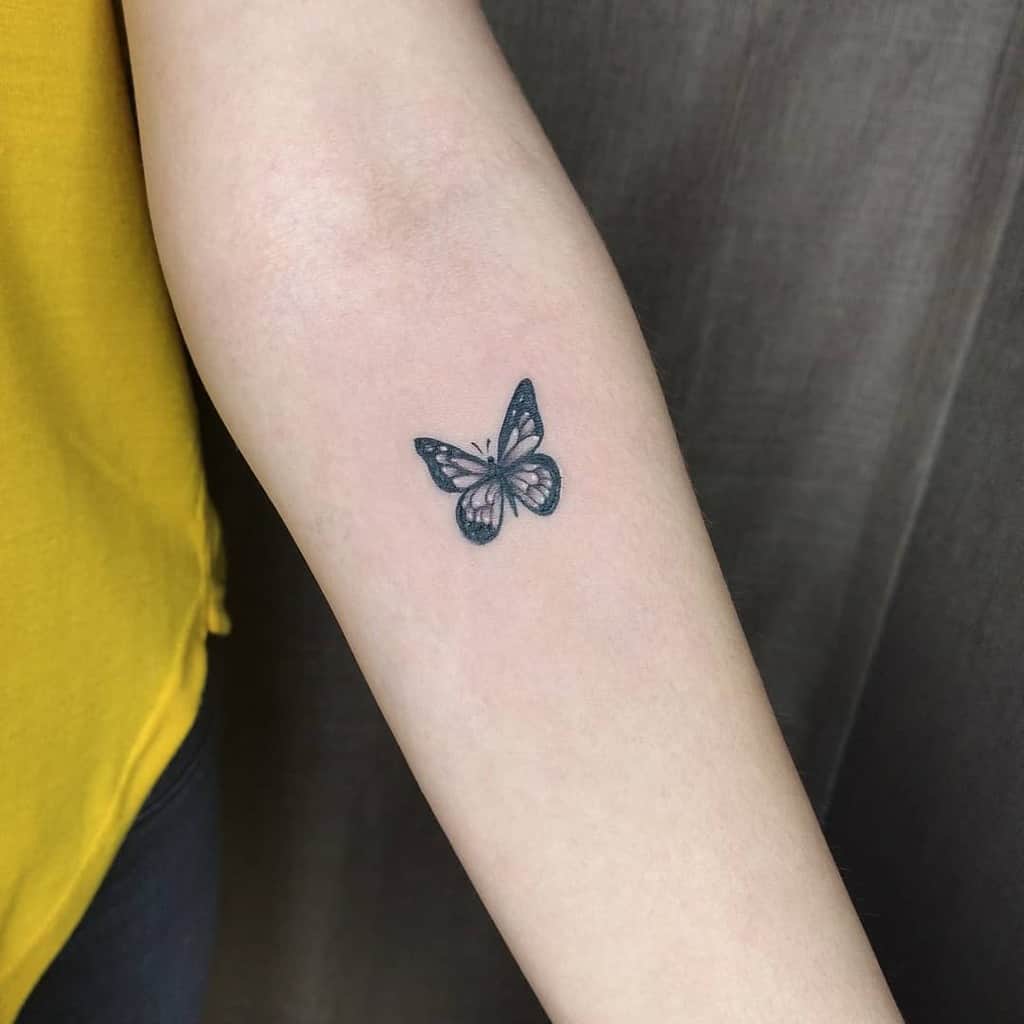 A small black and white butterfly tattoo on a woman's inner forearm