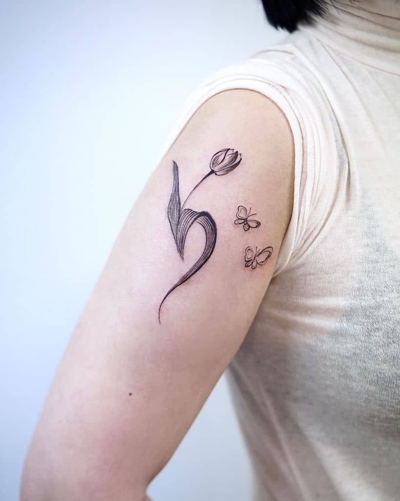 A delicate black-line tulip tattoo on the upper arm, featuring a flowing stem, elegant curves, and two small butterflies for a whimsical touch.