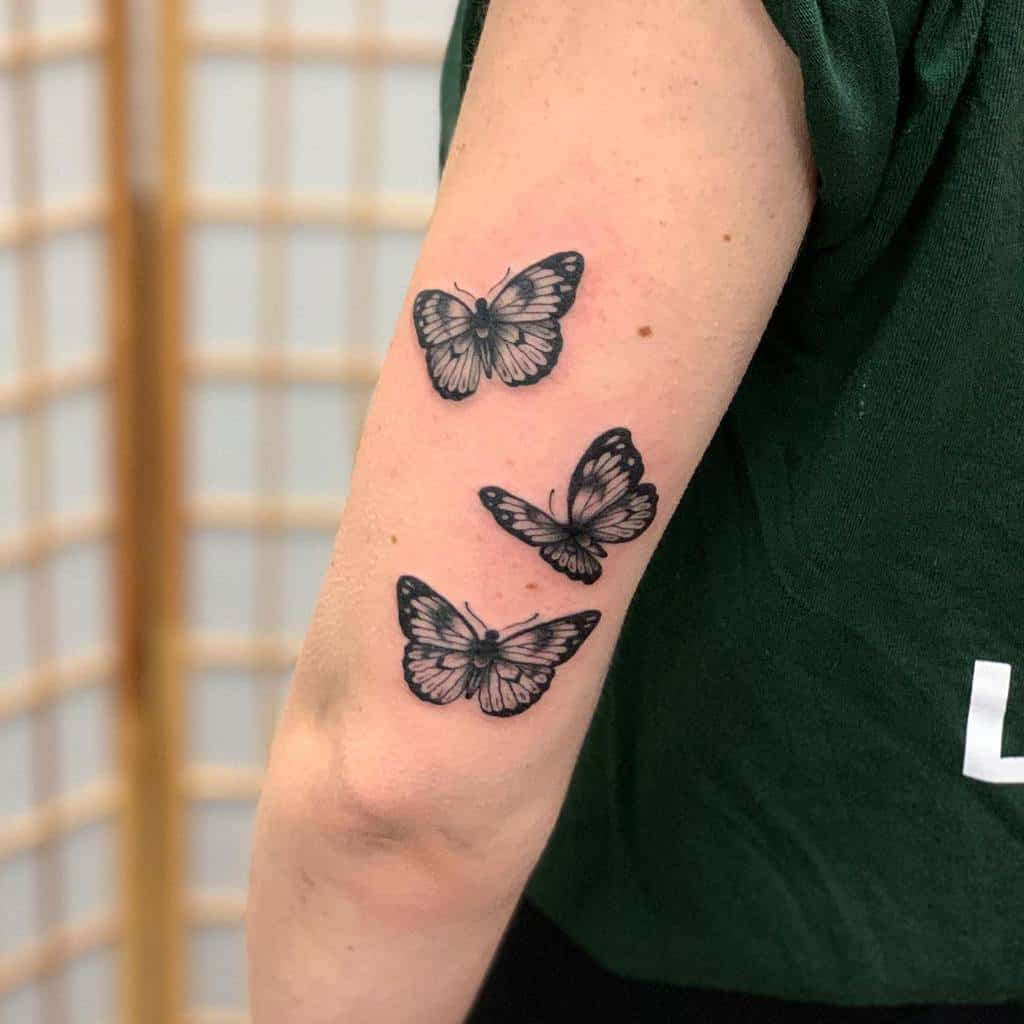 Tattoo of three black and white butterflies on a woman's upper arm