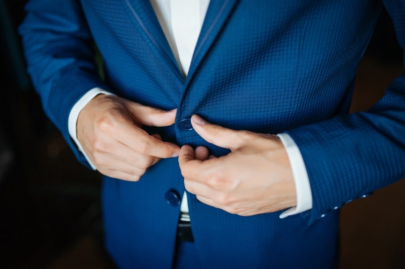 A person in a blue suit is buttoning up their jacket