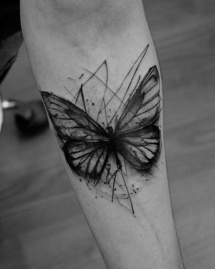 Abstract black ink butterfly tattoo on the forearm, featuring sketch-style lines and splattered shading for a raw, artistic effect.
