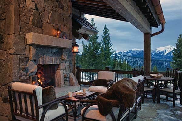 Rugged patio with stone fireplace, cozy seating, and snowy mountain view under a wooden pergola