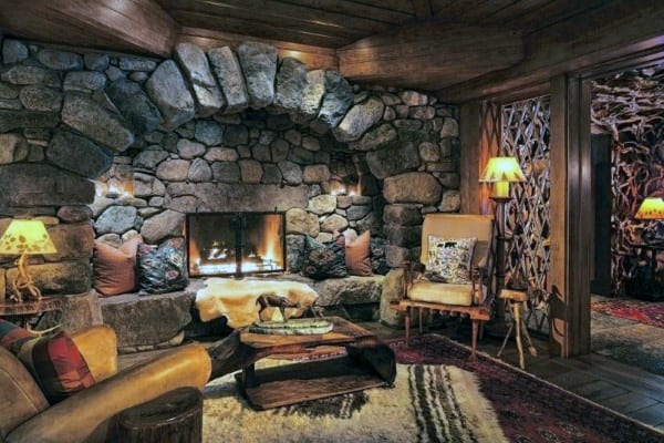 Rustic cabin living room with stone fireplace, cozy seating, and warm ambient lighting.