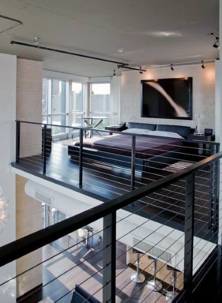 Modern loft bedroom with cable railing, dark flooring, and large wall-mounted TV.