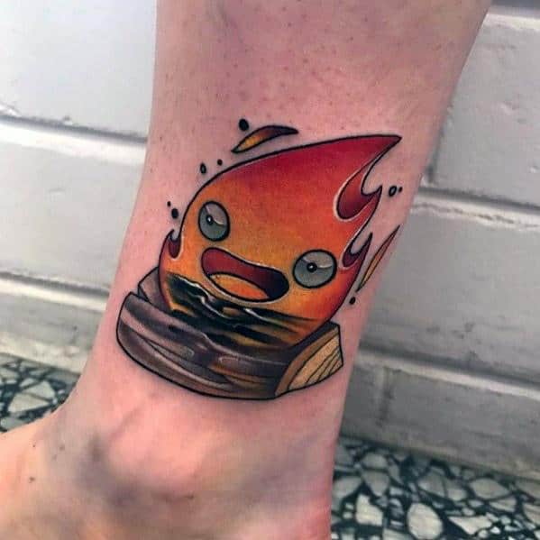 Colorful Calcifer tattoo with a dynamic flame shape, sitting on a log, wide-eyed with an open mouth and bold black outlines.