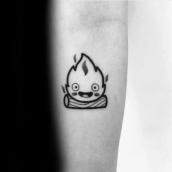 Minimal black line Calcifer tattoo with a happy face, simple flame outline, and log base on the inner forearm.
